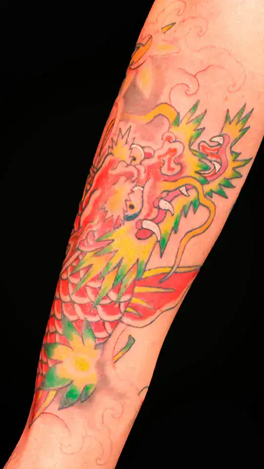 Tatuaje japonés de koi transformado en dragón con hojas momiji amarillas y rojas, realizado en el antebrazo con estilo tradicional por Nikko Quiroga.
